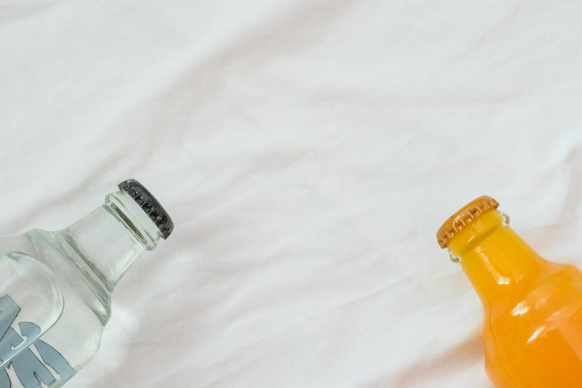 Bottles of Water and Orange Juice Lying on a White Sheet