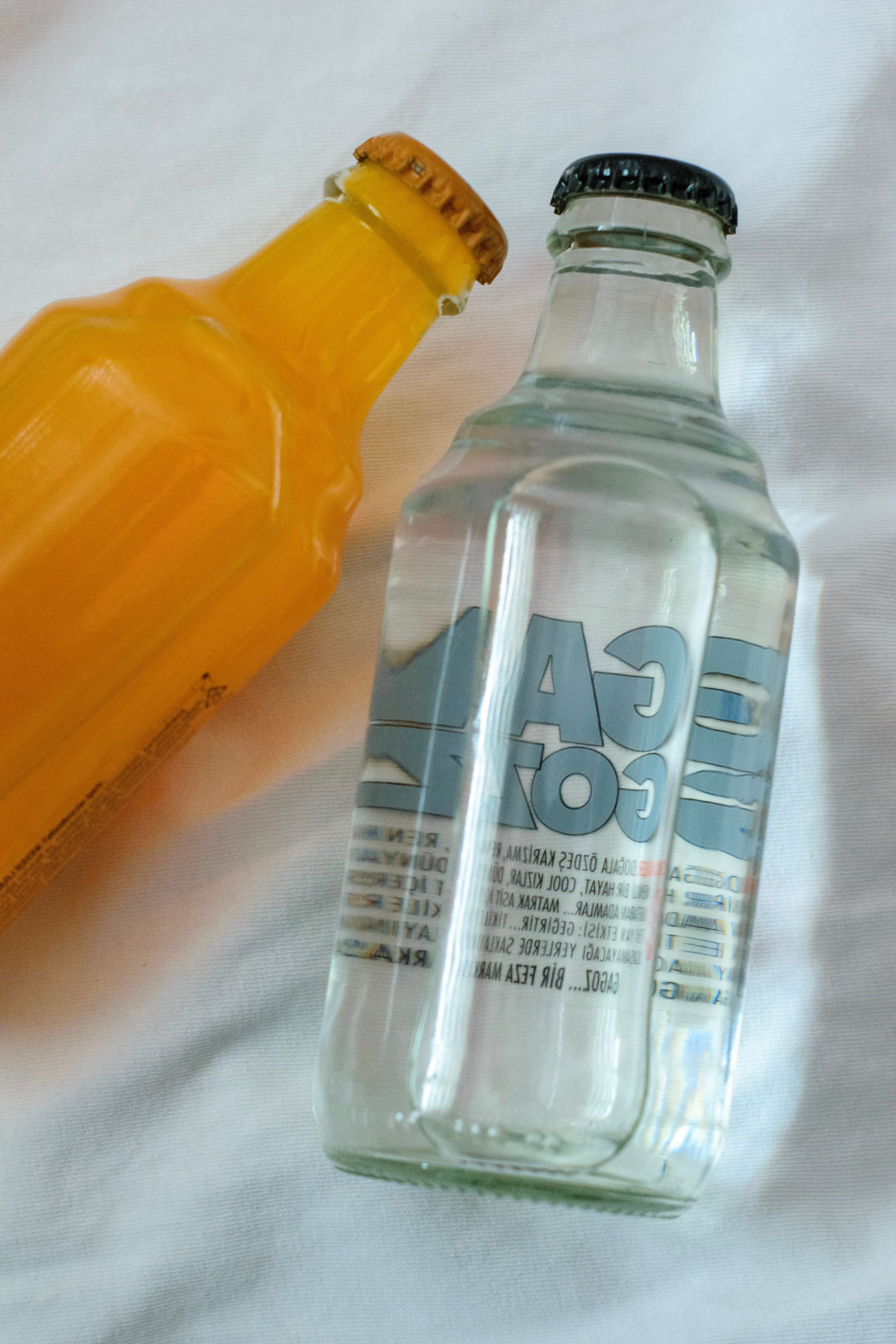 Bottles of Water and Orange Juice Lying on a White Sheet · Free Stock Photo