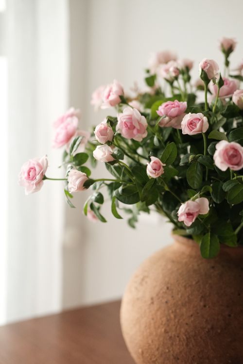 Free A delicate bouquet of pink roses in a rustic vase on a wooden table. Stock Photo