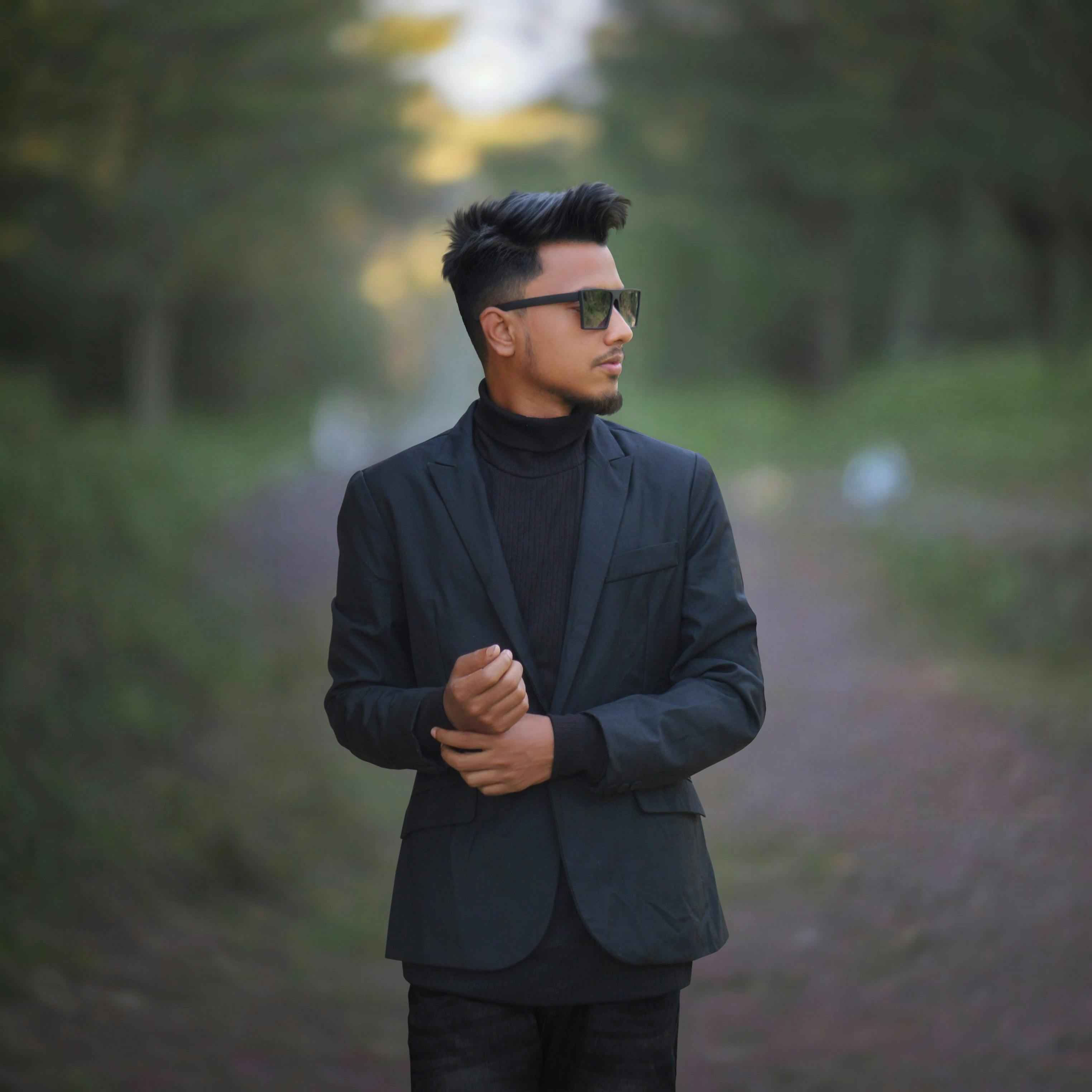 Stylish man in black suit and sunglasses posing outdoors in Sylhet.
