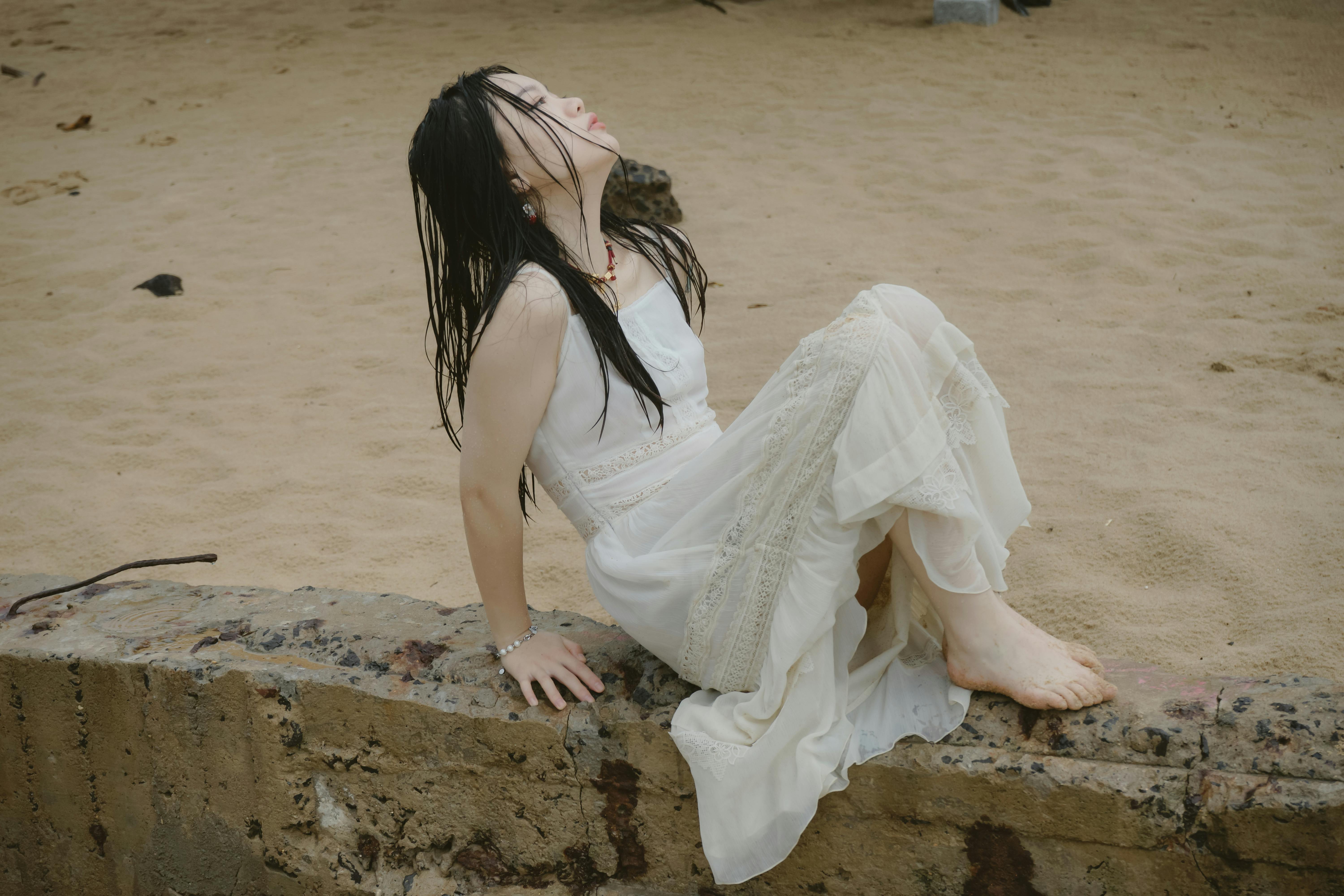 Calm pose of woman in white dress by the beach, showcasing elegance.