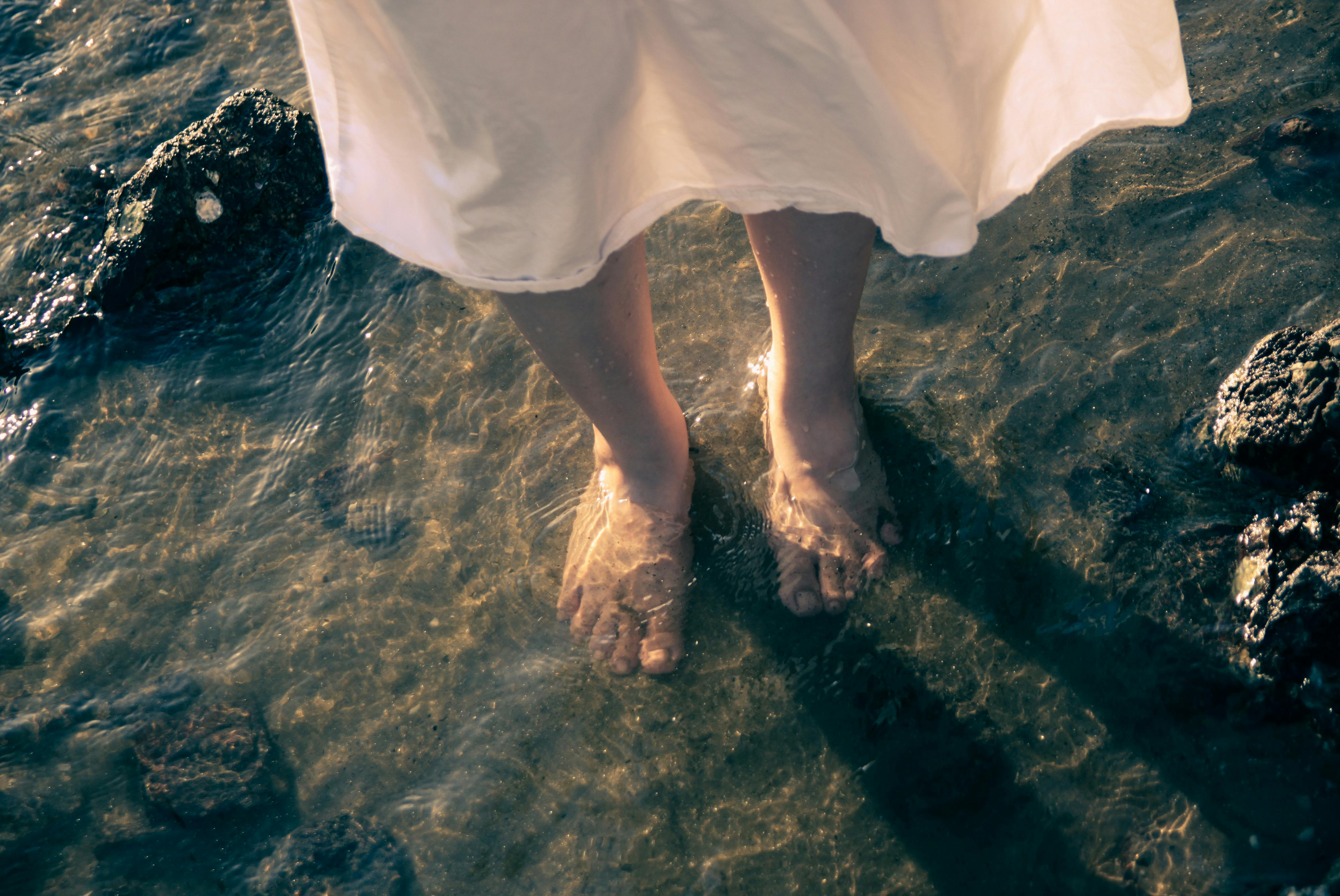 Woman's feet in water among rocks, creating a serene and peaceful scene.