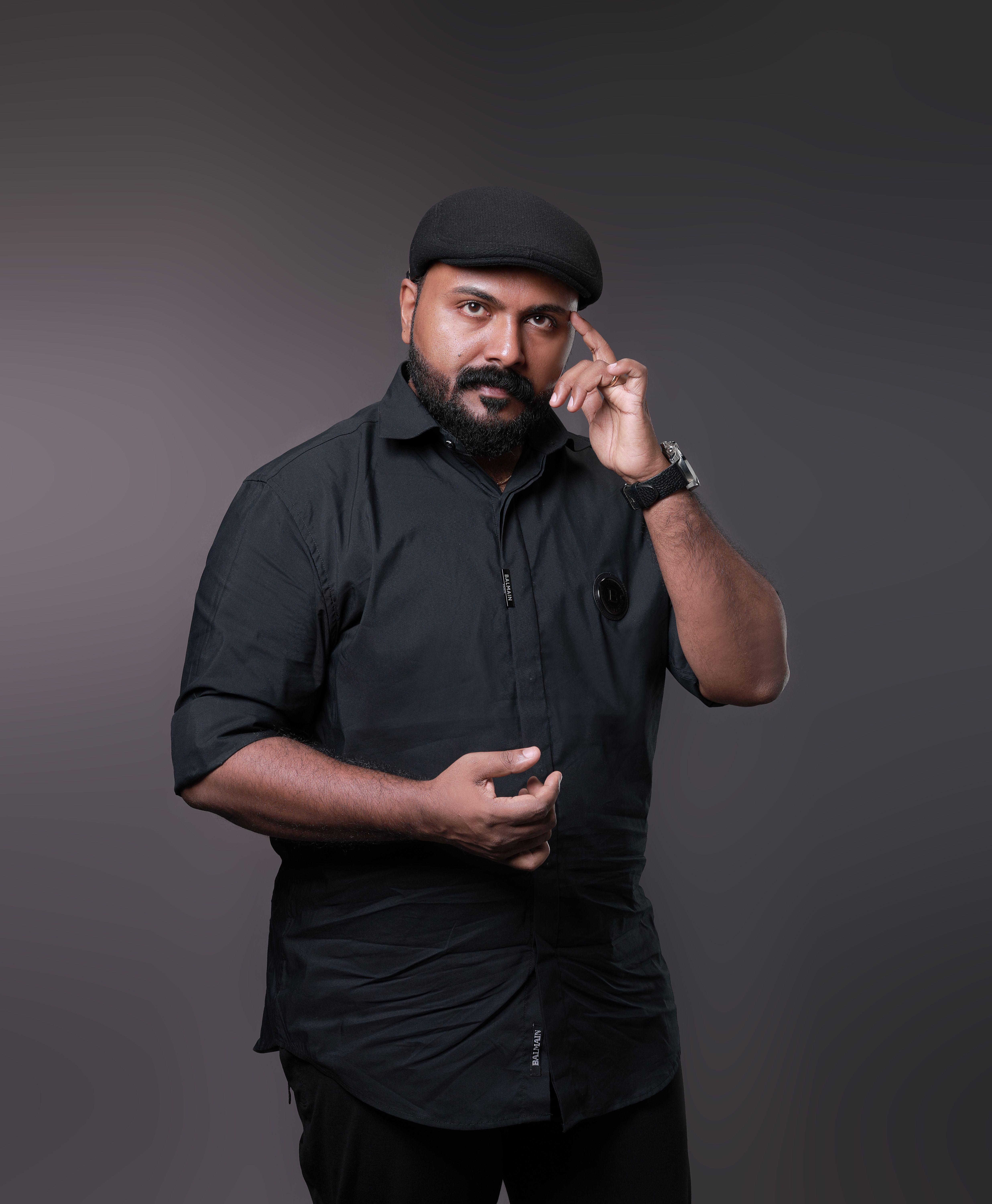 Portrait of a man in black attire and hat, posing thoughtfully in a studio.