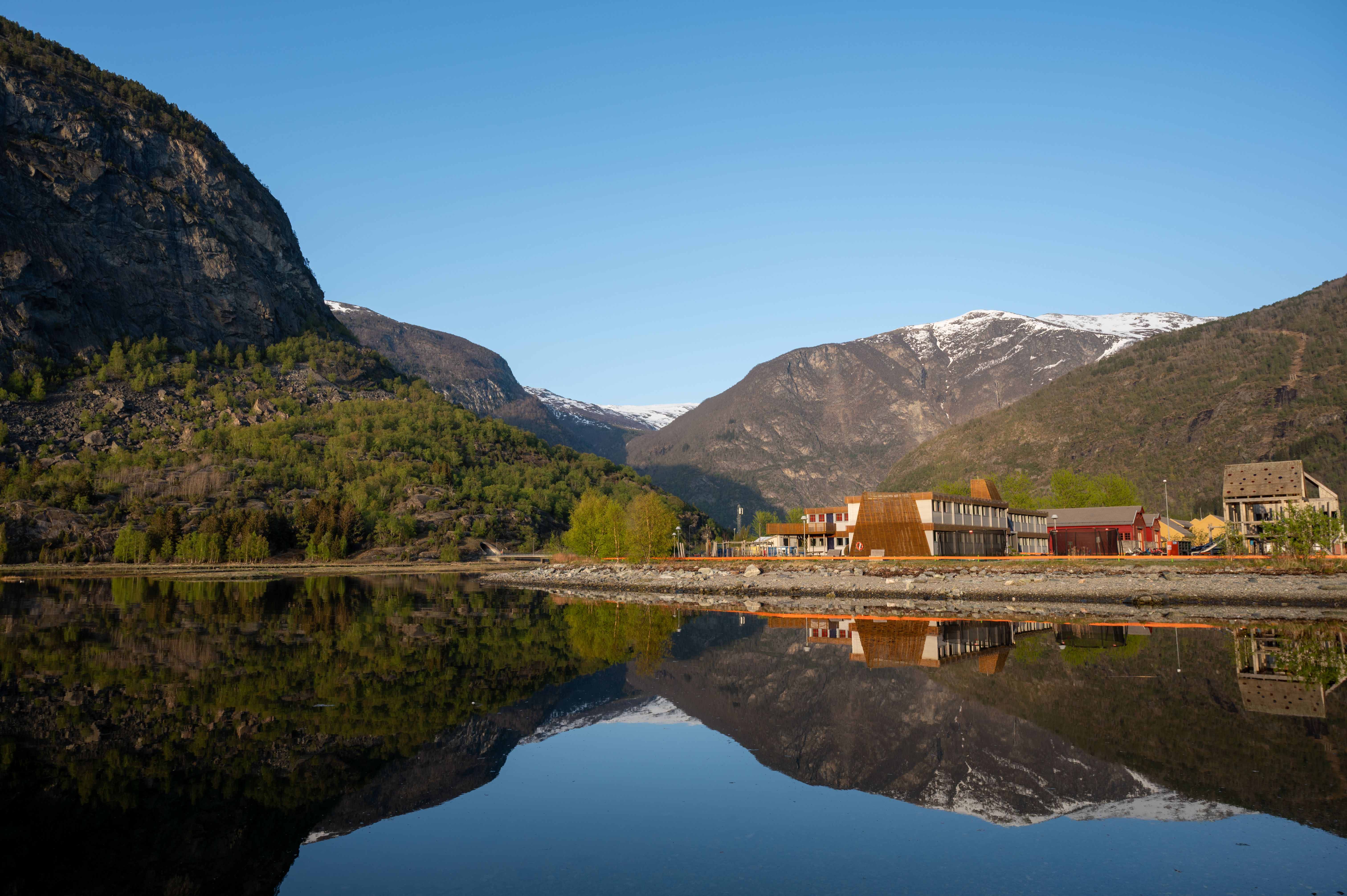 Reflective landscape of Aurlandsvangen village with tranquil waters and surrounding mountains in spring.