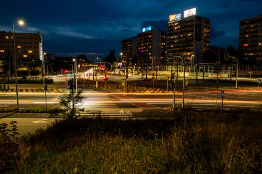 A vibrant city intersection at night features light trails and illuminated buildings.