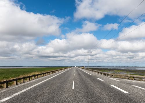 Free Empty countryside road in Rømø, Denmark stretching into the horizon under a vibrant cloudy sky. Stock Photo