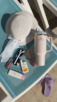 Flat lay of summer accessories on a sunbed, featuring a hat, sunscreen, and stylish bottle.
