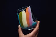 深色背景上，一只手握着玻璃的特写，呈现出鲜艳的彩虹色