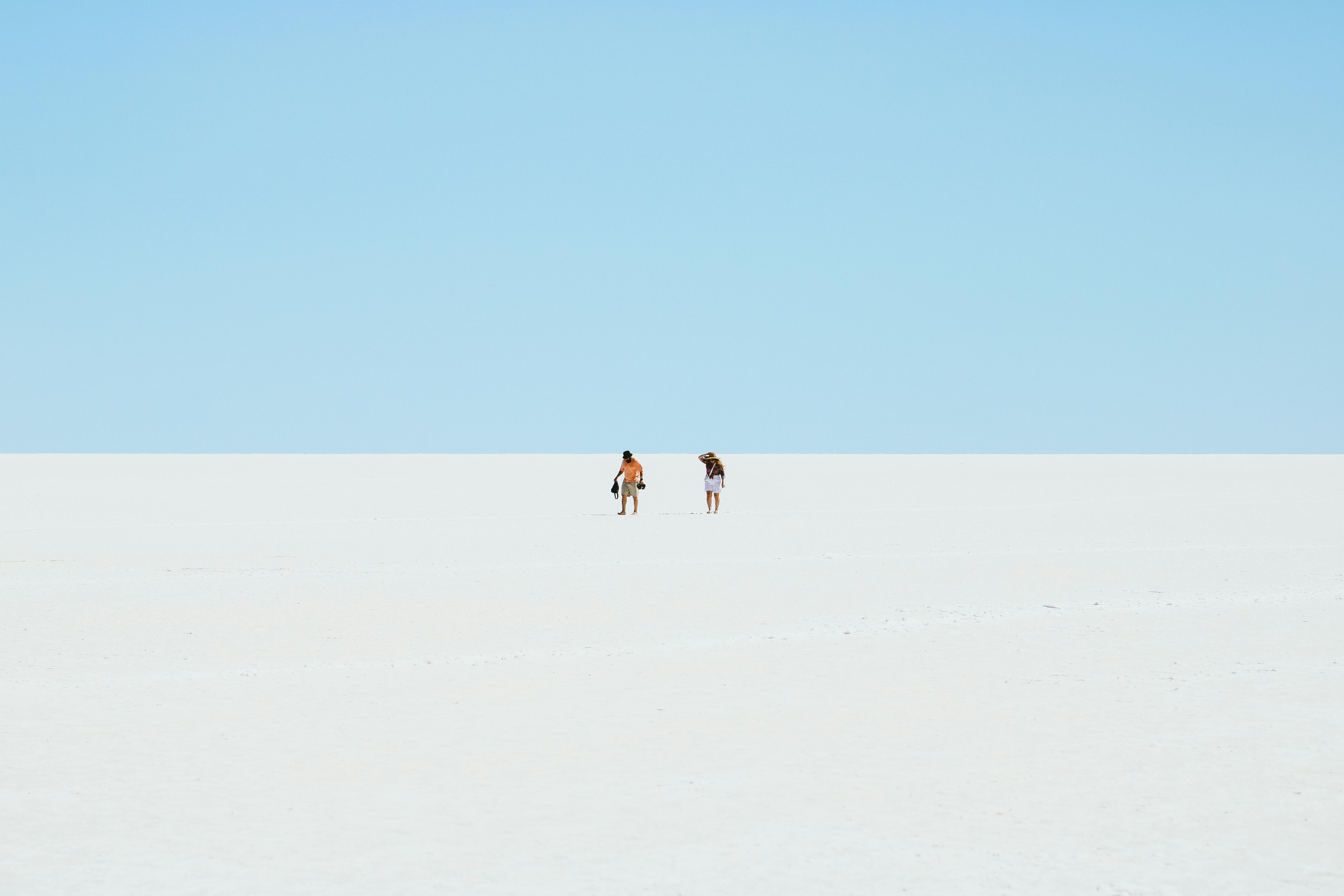 two people walking on a salt flat in the distance