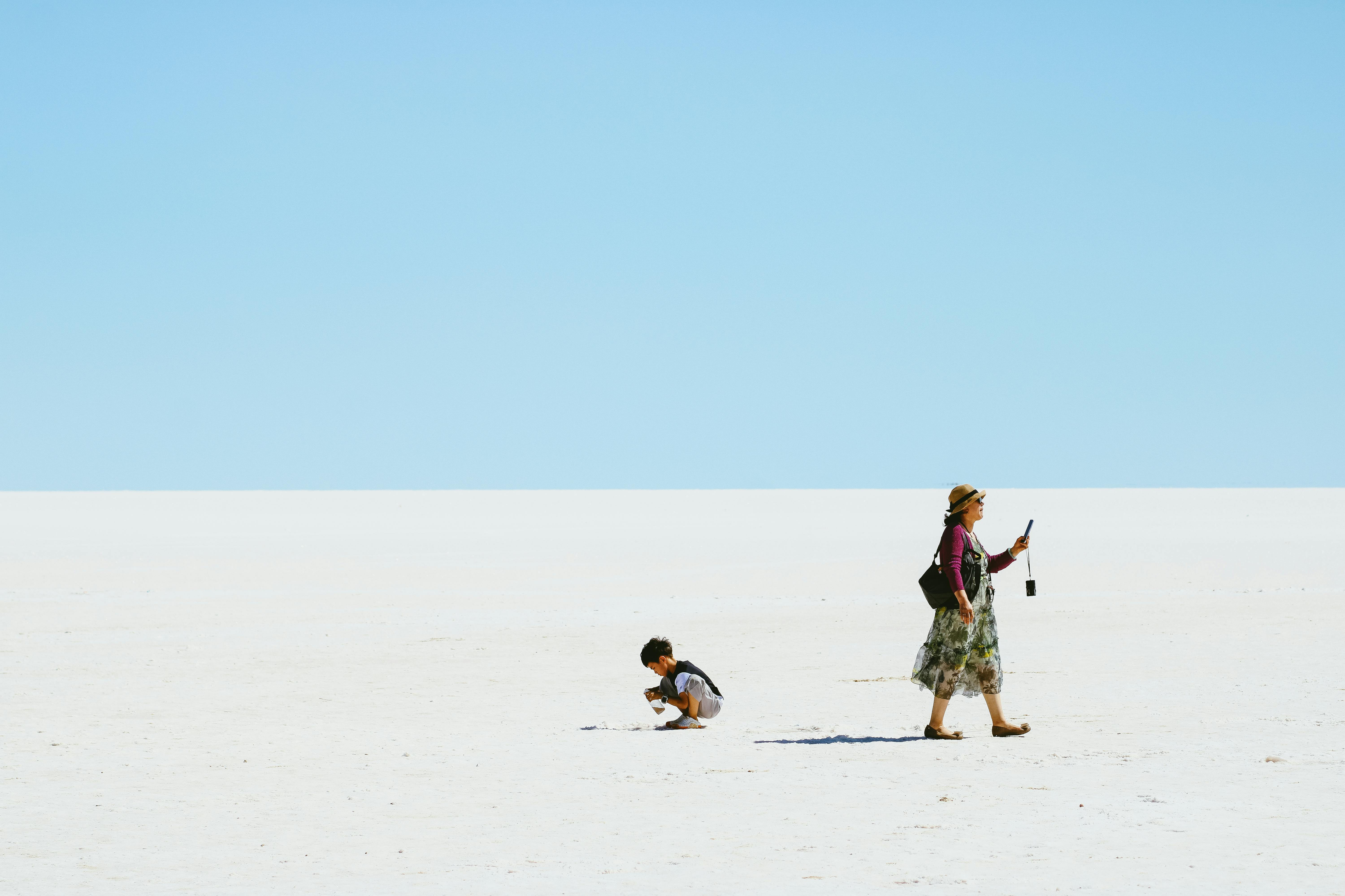 A woman and child enjoying a sunny day on a vast sandy terrain under a clear blue sky.
