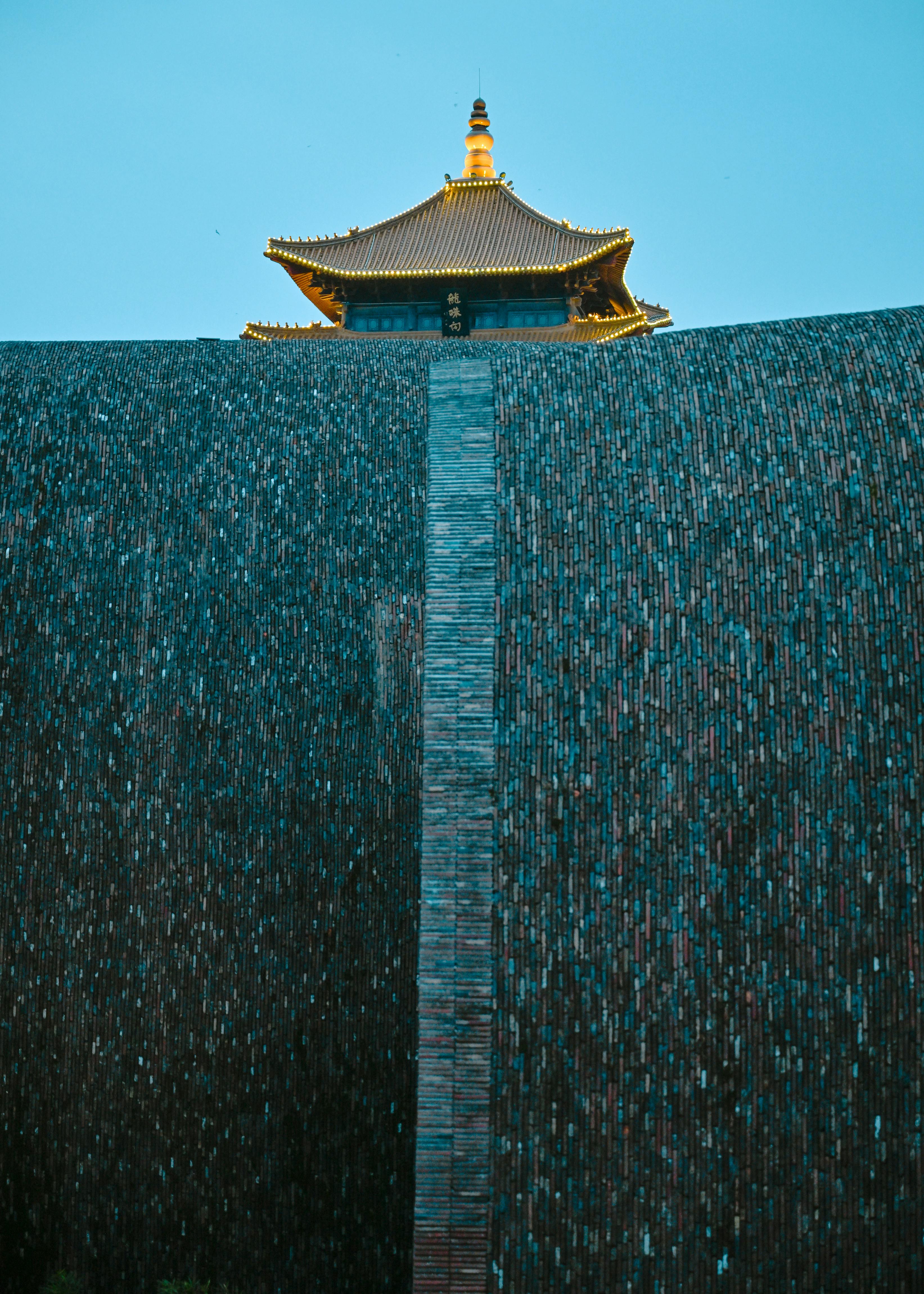 A stunning view of a traditional pagoda tower rising above a textured wall against a clear sky.