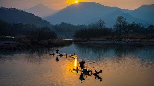 Free Silhouette of fishermen casting nets at sunset on a serene lake surrounded by mountains. Stock Photo