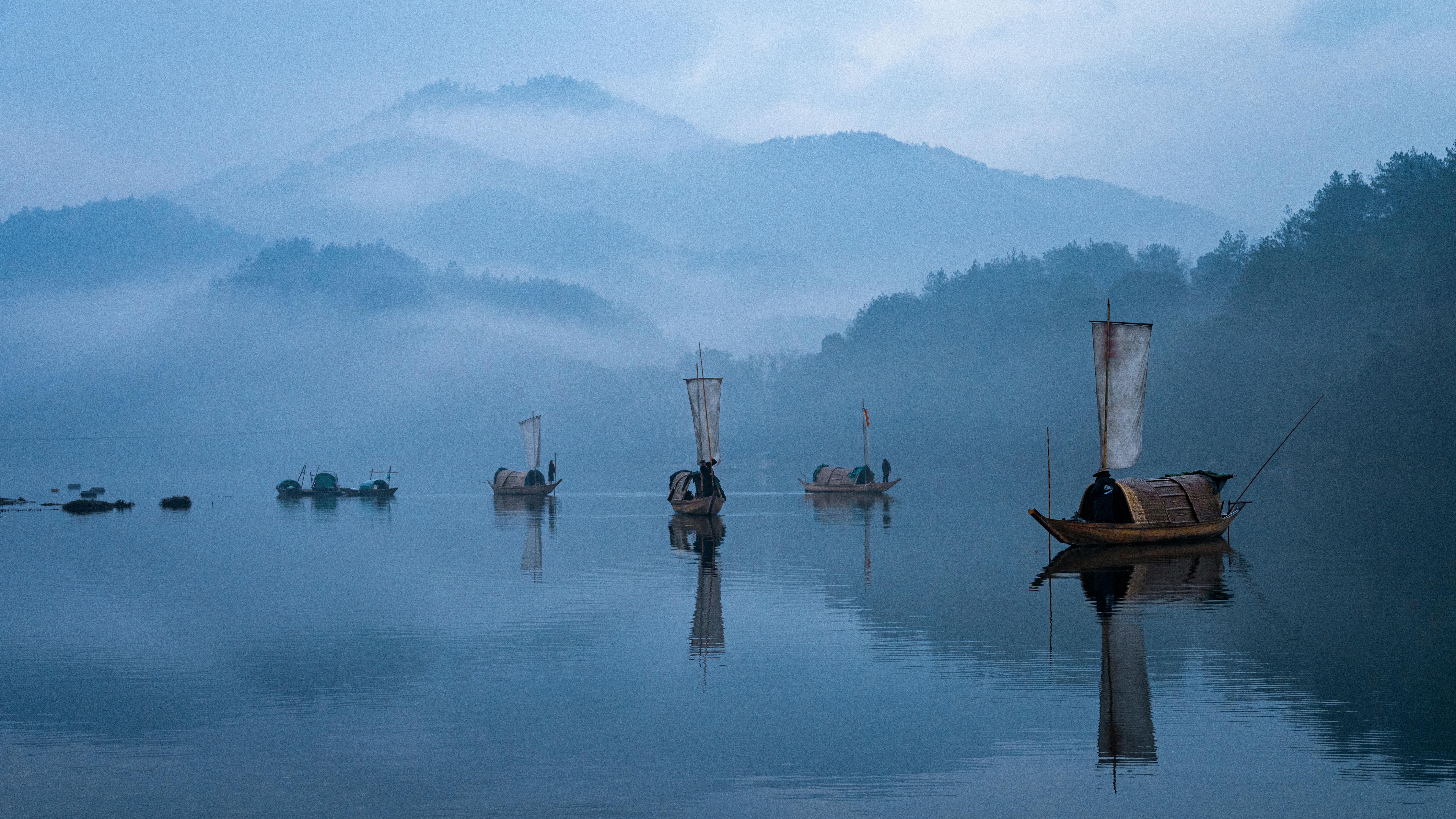 Scenic view of traditional boats on a misty lake surrounded by foggy hills.