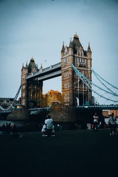 Stunning vertical shot of London's Tower Bridge with people by the Thames.