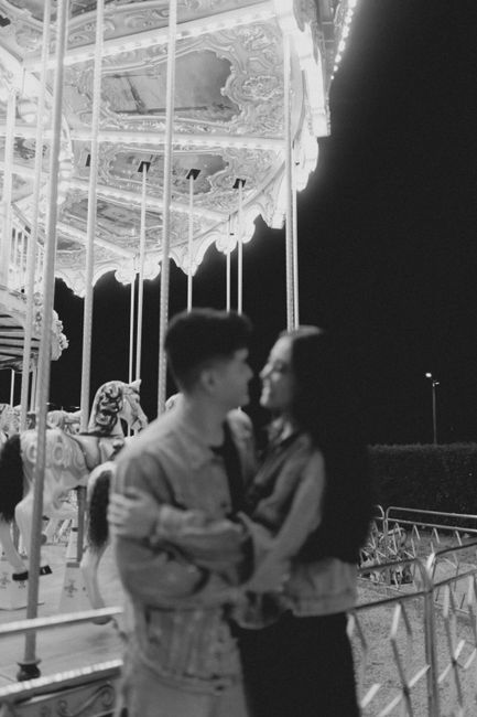 Young couple embracing near a lit carousel at night, capturing joyful moments.