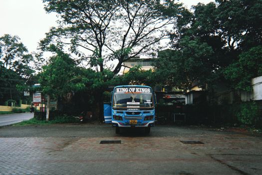 A blue bus labeled 'King of Kings' parked in an urban, tree-lined area.