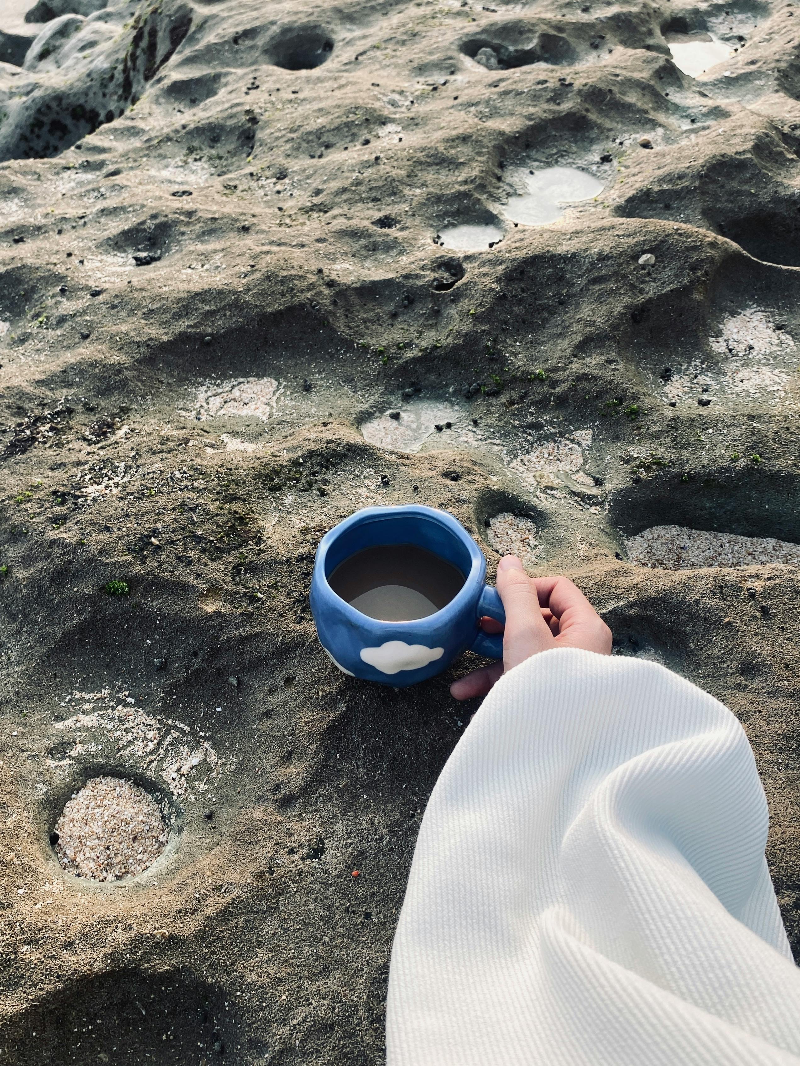 A cozy moment holding a blue cloud cup on a unique rock terrain in Malang, Indonesia.