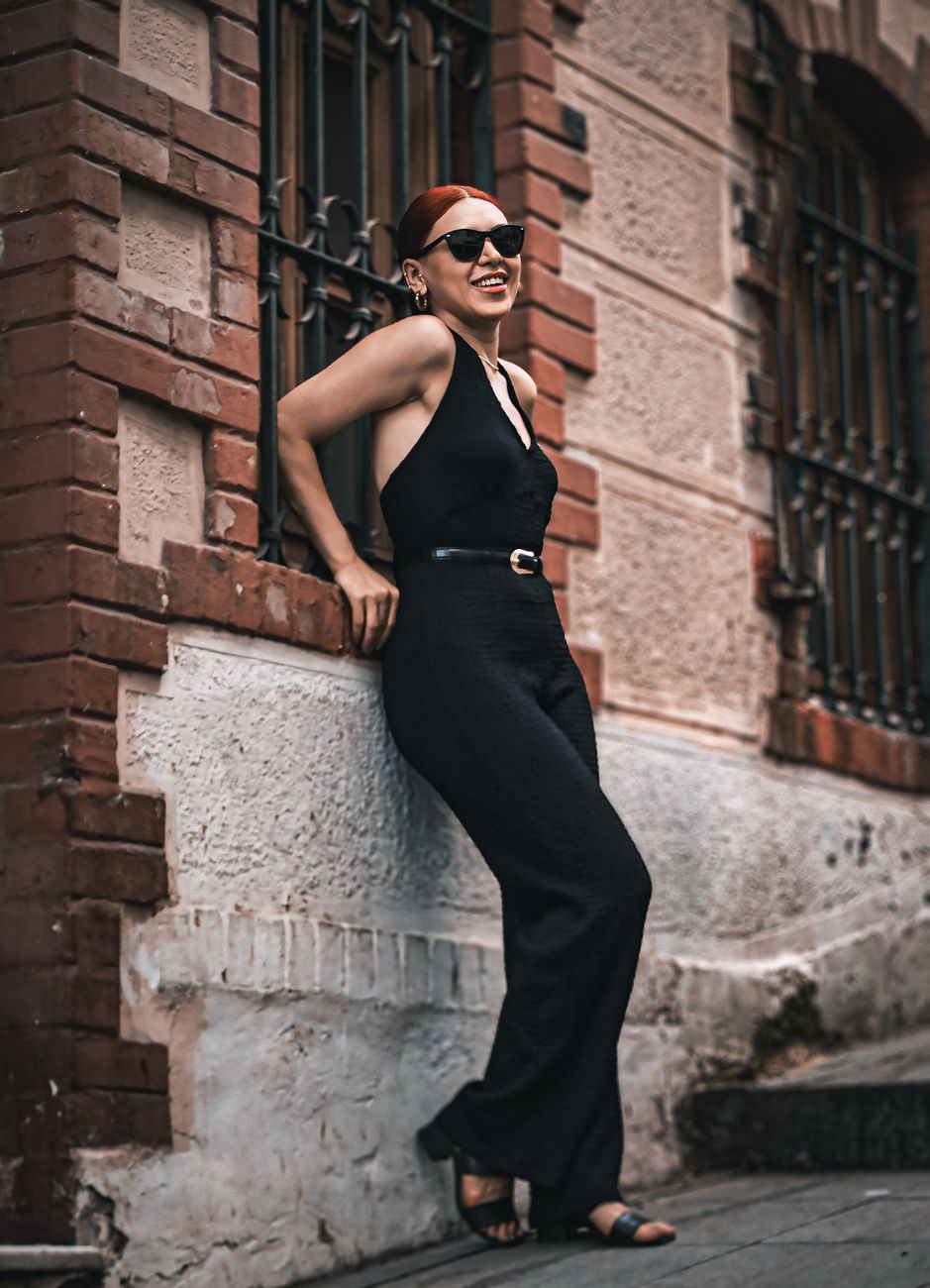 Chic woman in black outfit and sunglasses leaning against a brick wall in a city street, exuding confidence.