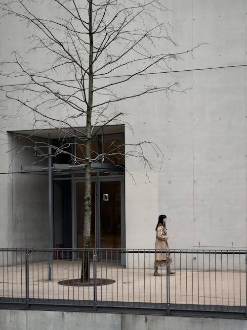 A woman walks past a tree in front of a building