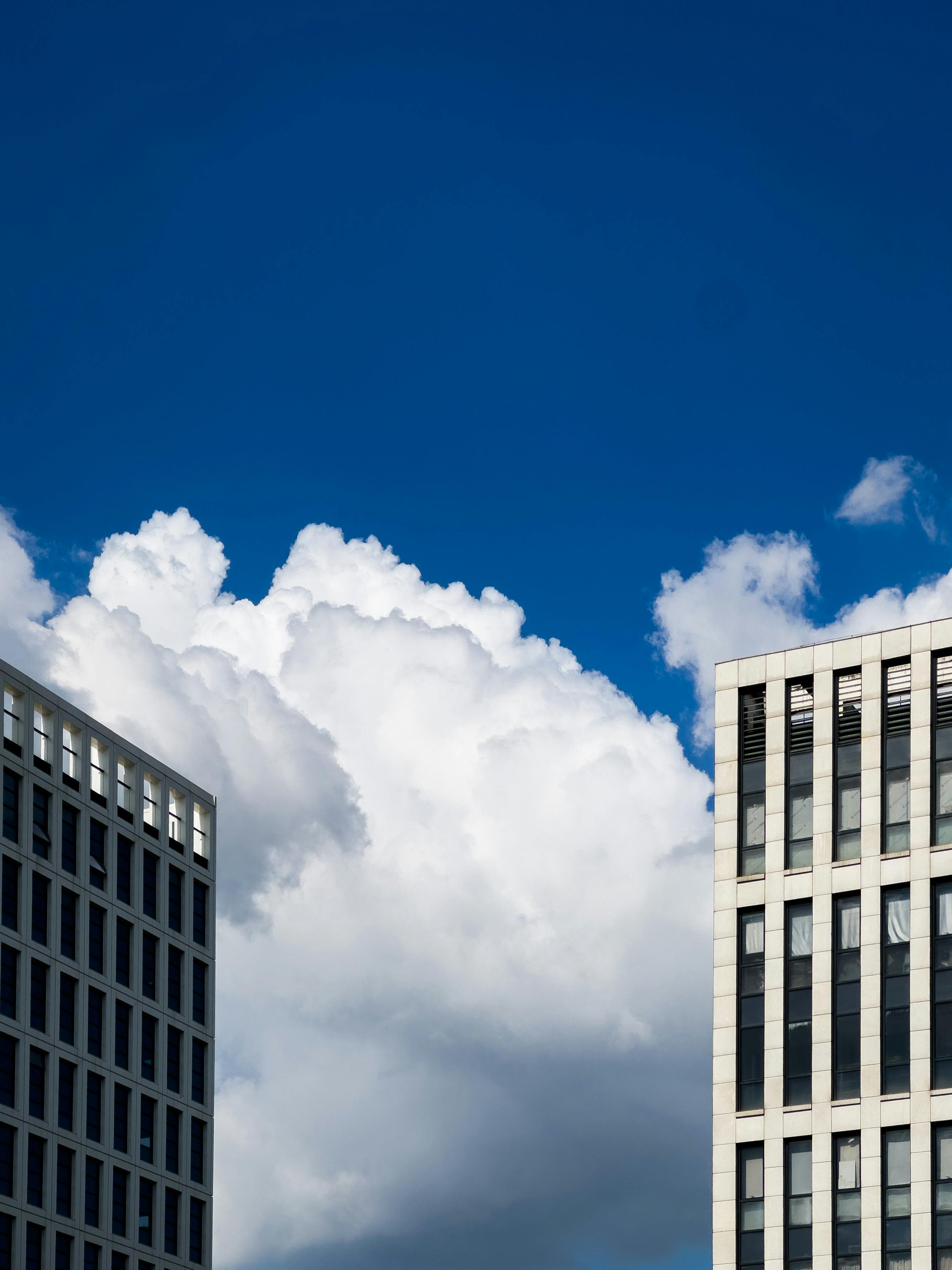 Contemporary skyscrapers frame a vibrant blue sky with fluffy clouds.