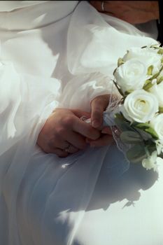 Close-up of a bride's hands holding a white floral bouquet in soft lighting.