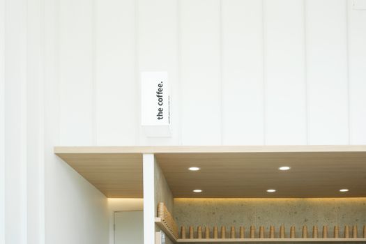 Minimalist coffee shop interior with wooden shelf and modern lighting, featuring stacked cups.