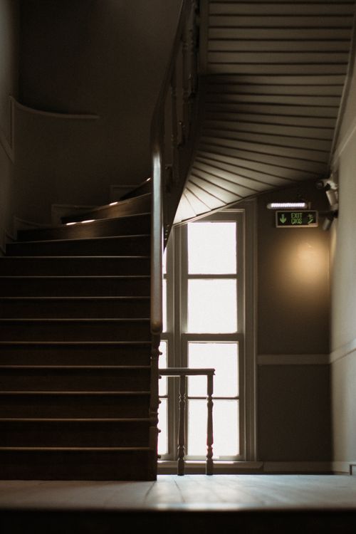 Free A beautifully lit spiral staircase next to a large window in a quiet hallway. Stock Photo