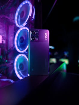Smartphone illuminated by vibrant purple lighting next to illuminated PC hardware.