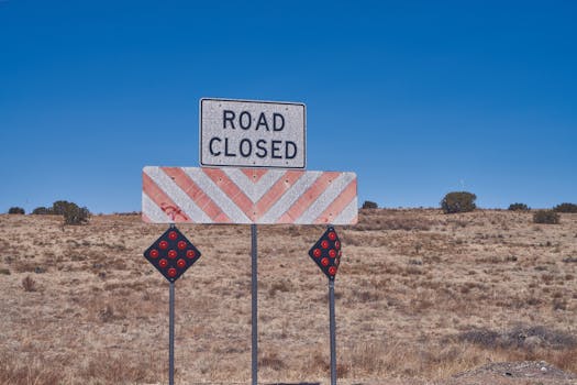 Road closed sign in a dry, desert setting under a clear blue sky, symbolizing detour or restriction.