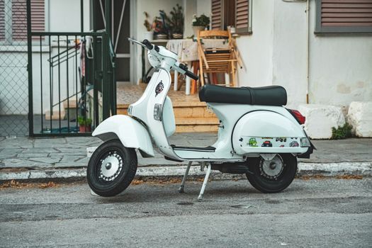 Classic white Vespa scooter parked in front of a house in Greece. Urban street scene.
