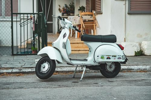 Free Classic white Vespa scooter parked in front of a house in Greece. Urban street scene. Stock Photo