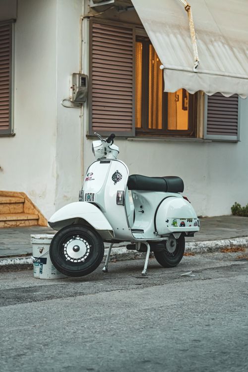 Free A classic white scooter parked on a quaint Greek street near a charming house. Stock Photo