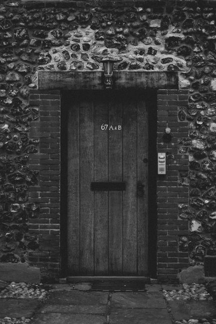 Black and white photo of a wooden door set in a rustic stone wall.