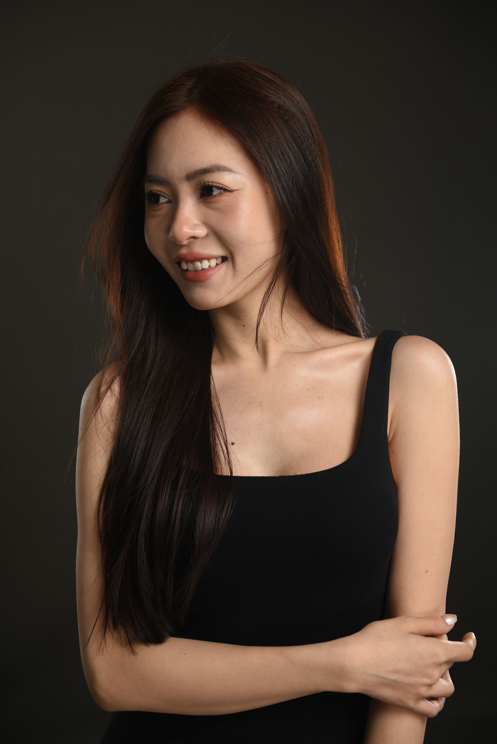 Captivating studio portrait of a smiling woman with long hair and a black tank top.