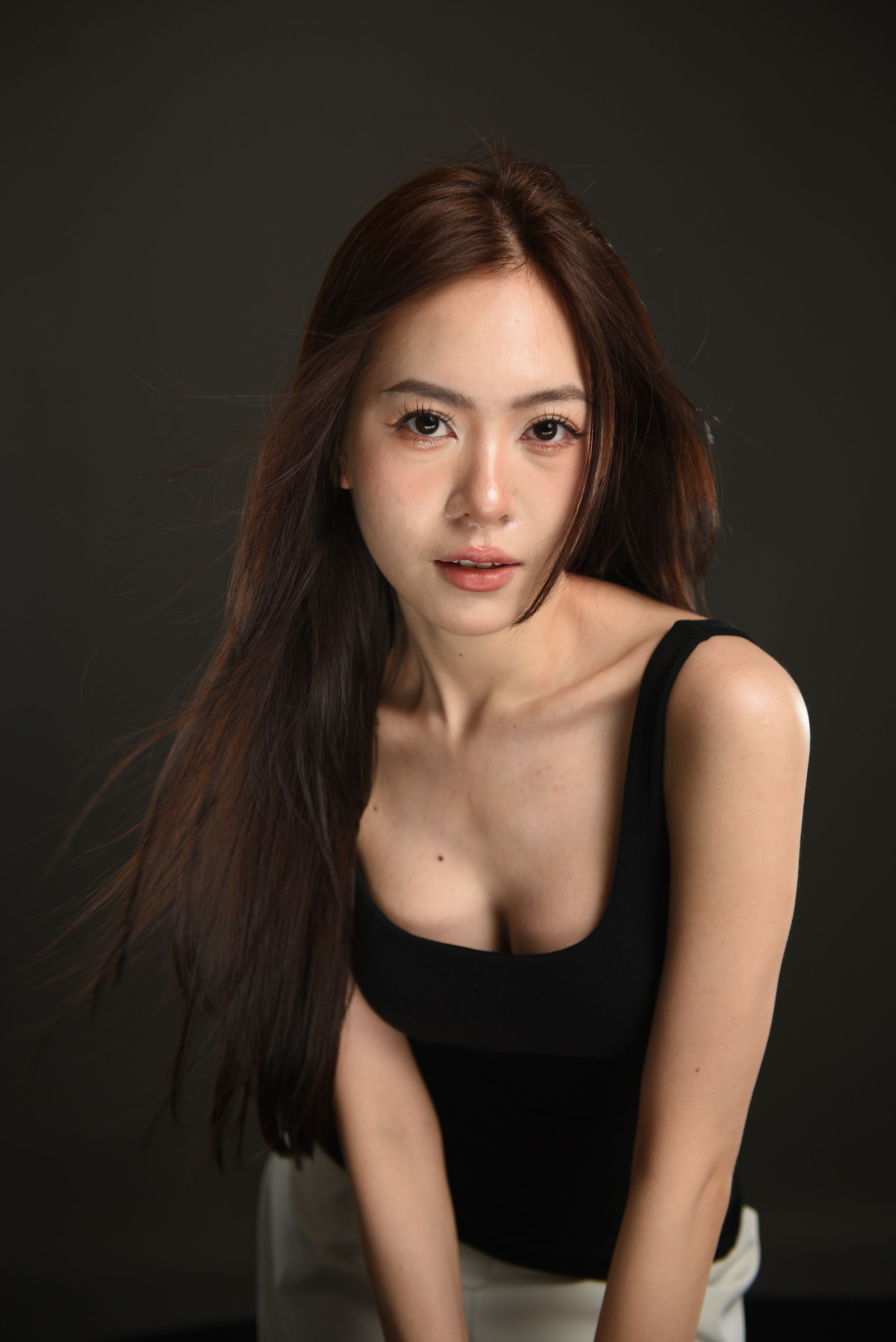 Stylish studio portrait of a woman posing in a black top with flowing hair.
