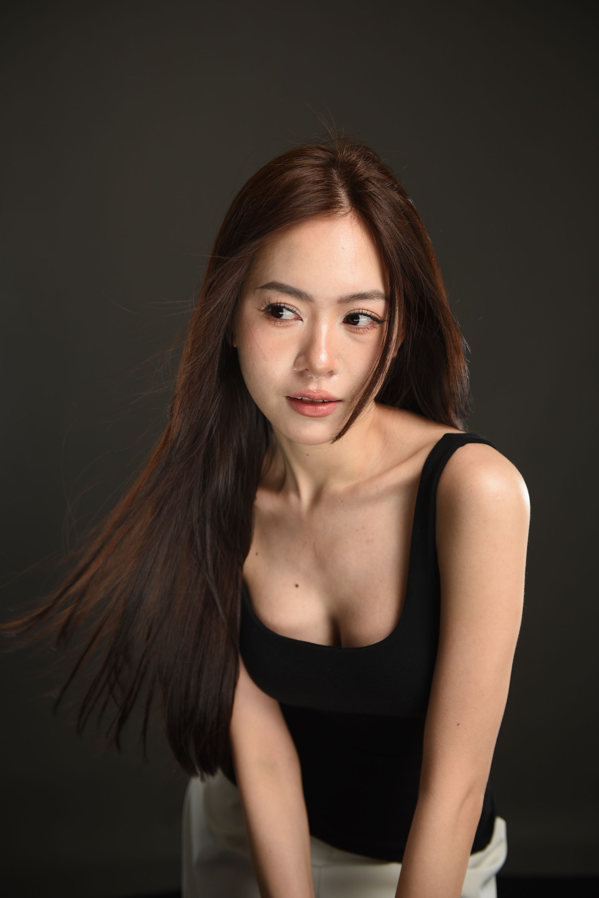 Portrait of an Asian woman with long brown hair in a studio setting, wearing a black tank top.