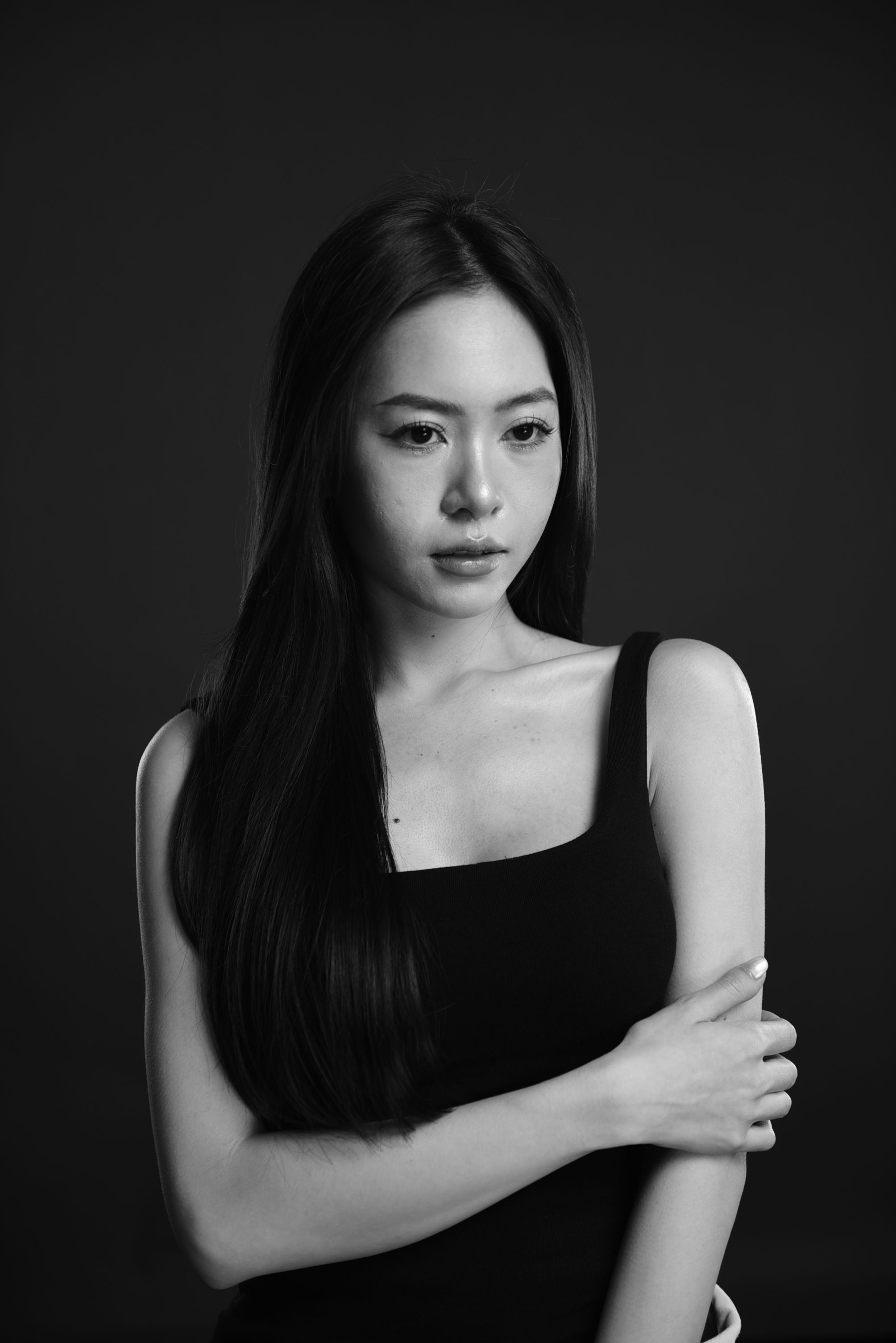 A stunning black and white studio portrait of a woman with long hair in a tank top.