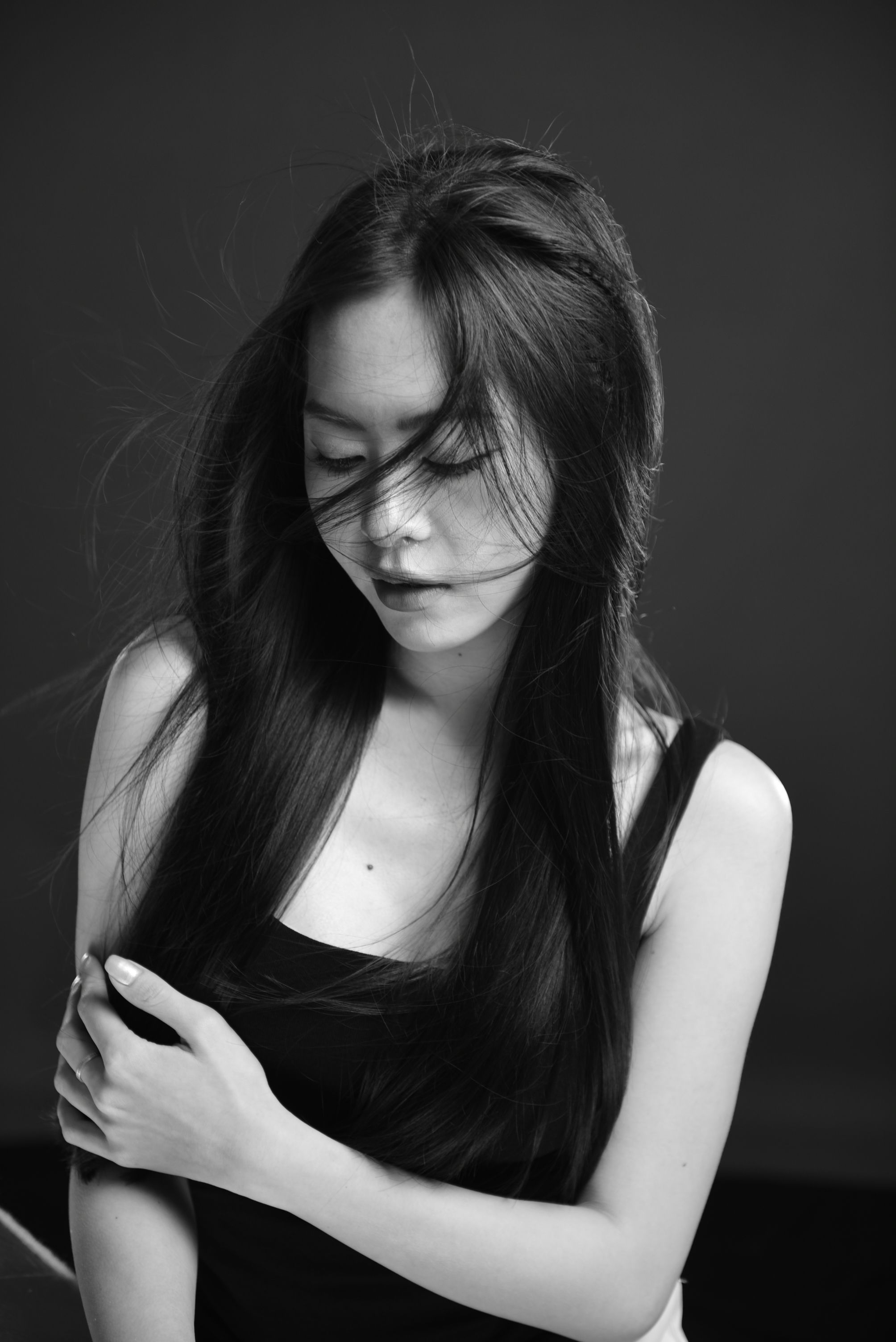 Artistic black and white portrait of a woman with long hair, arms crossed, looking down.