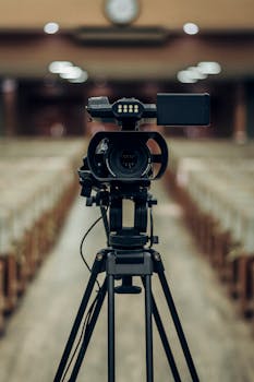 Front view of a professional video camera on a tripod in an empty auditorium.