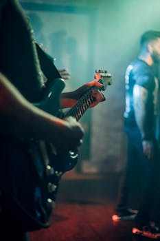 Guitarist playing electric guitar on stage during a live rock band performance with vibrant lighting.