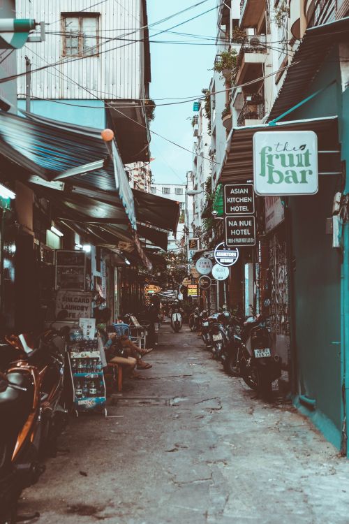Free Narrow city alley with vibrant shops and cafes under awnings, featuring urban charm and street life. Stock Photo