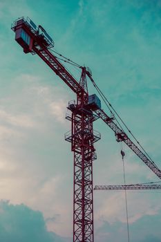 A tall red tower crane at a construction site against a clear sky, depicting urban development.