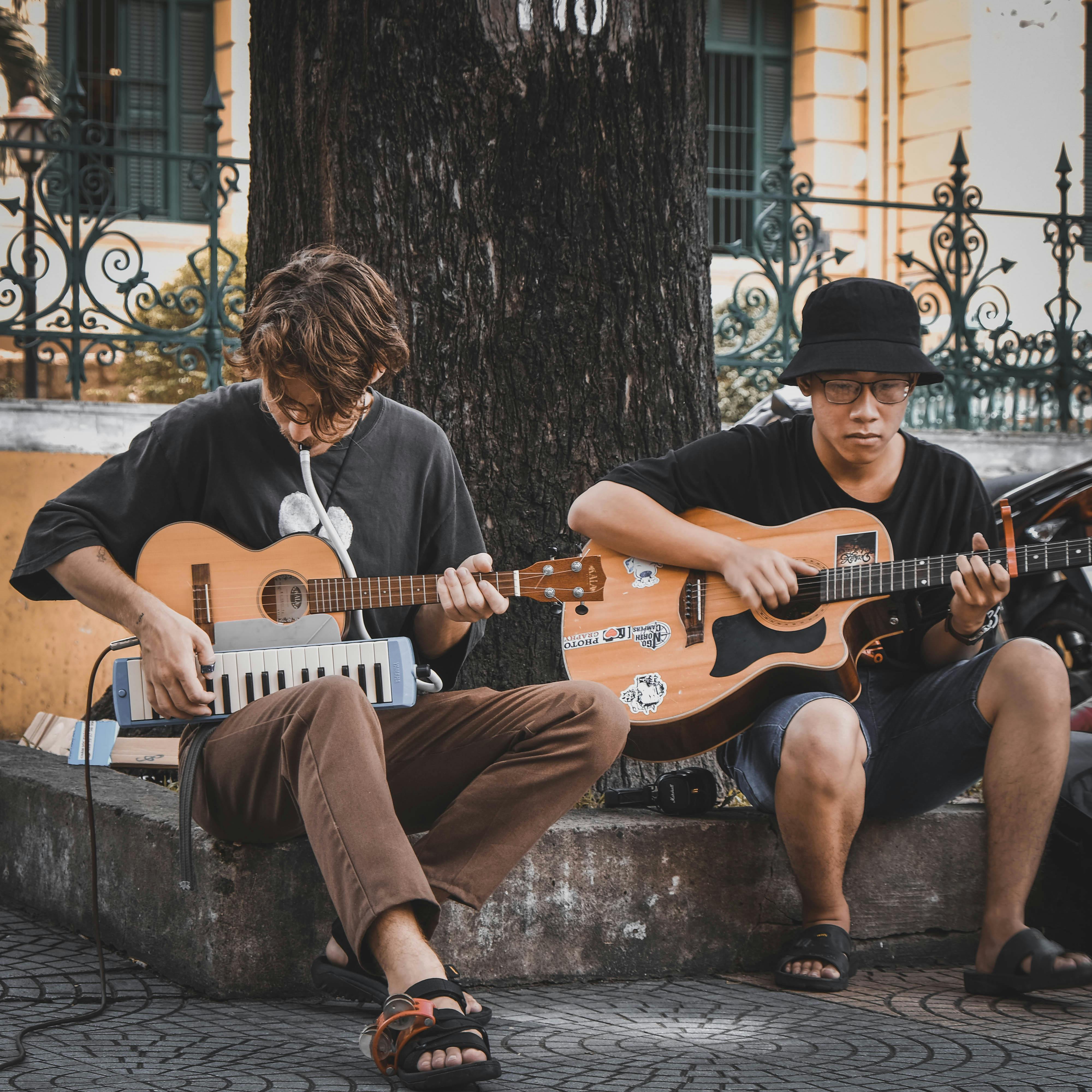 Two street musicians playing acoustic guitars in an urban setting, creating a lively atmosphere.