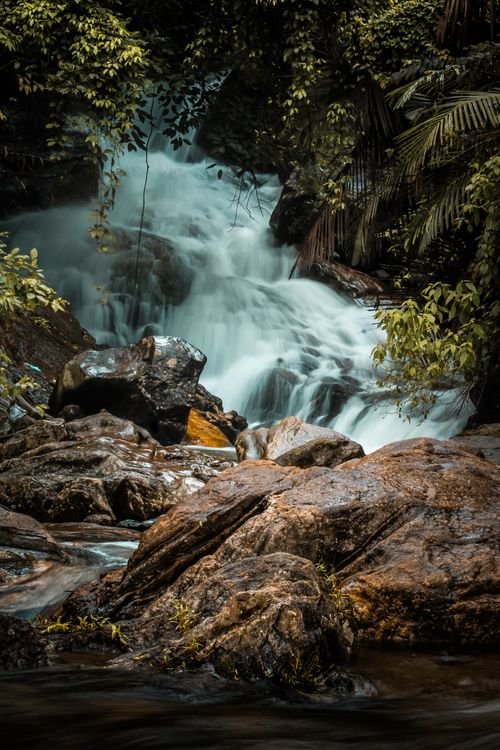 Free Beautiful waterfall flowing gently through a lush tropical forest, surrounded by rocks and greenery. Stock Photo
