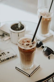 Refreshing iced coffee on a minimalistic table with sunlight and sunglasses. Perfect summer morning vibe.