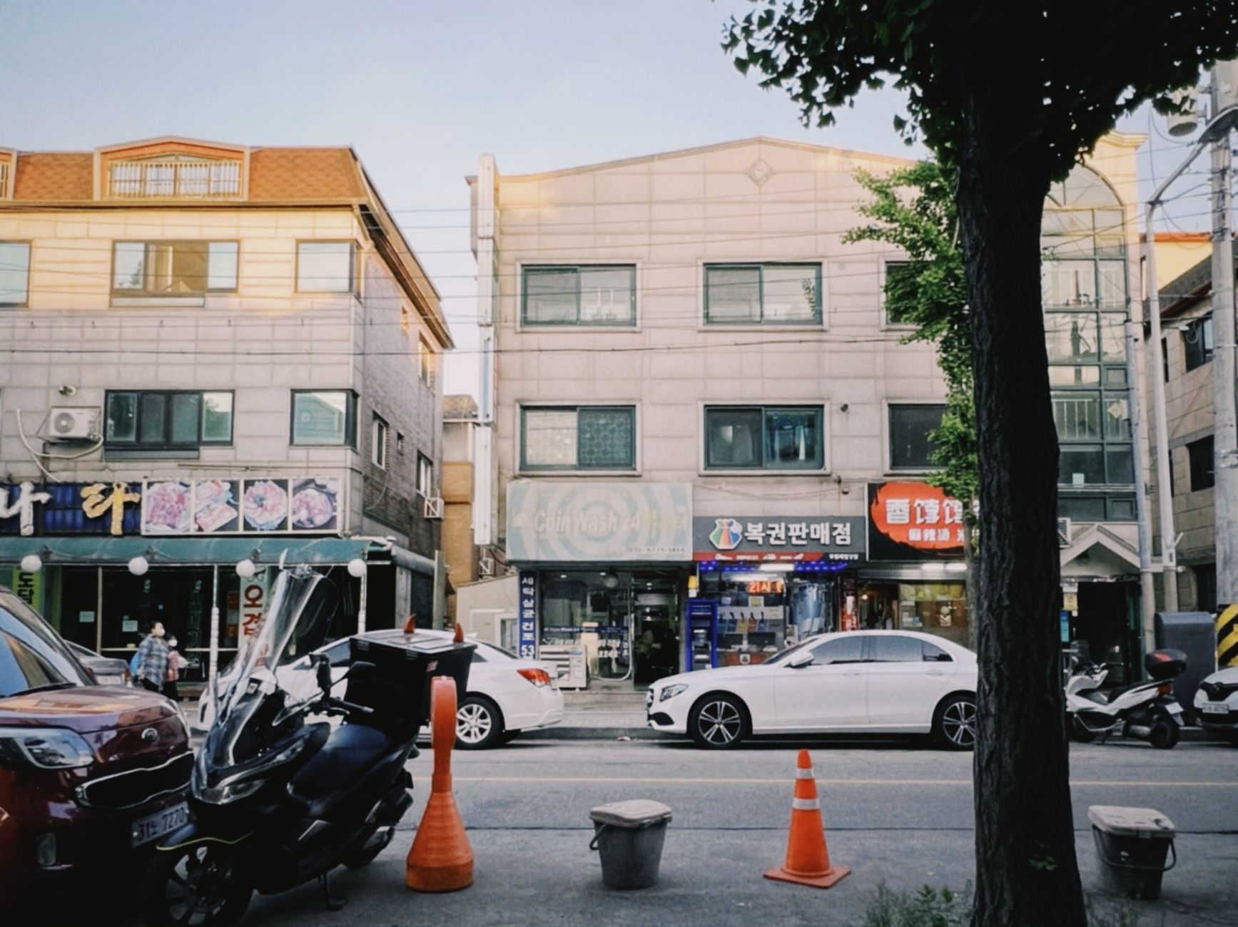 Bustling street view in Ansan-si, South Korea, featuring traffic, shops, and buildings on a sunny day.