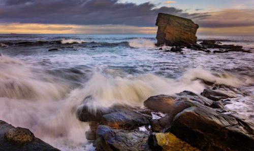 Free Dramatic waves crash along the coastal rocks at sunset, showcasing nature's power. Stock Photo