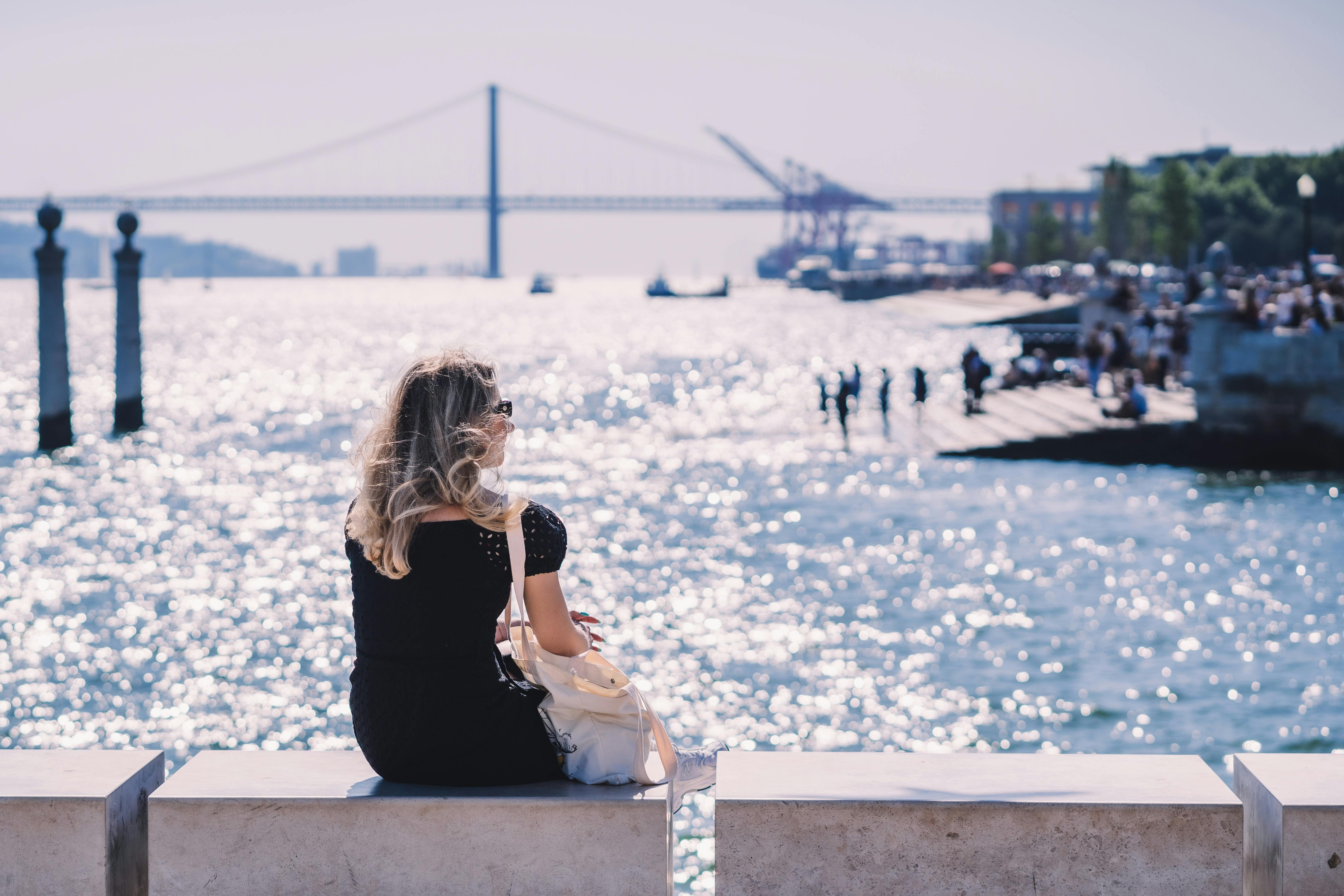 blonde woman in black dress sitting on wall over river