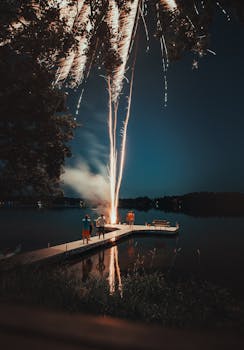 宁静的湖面上，绚丽的烟花照亮夜空，人们在码头驻足观看