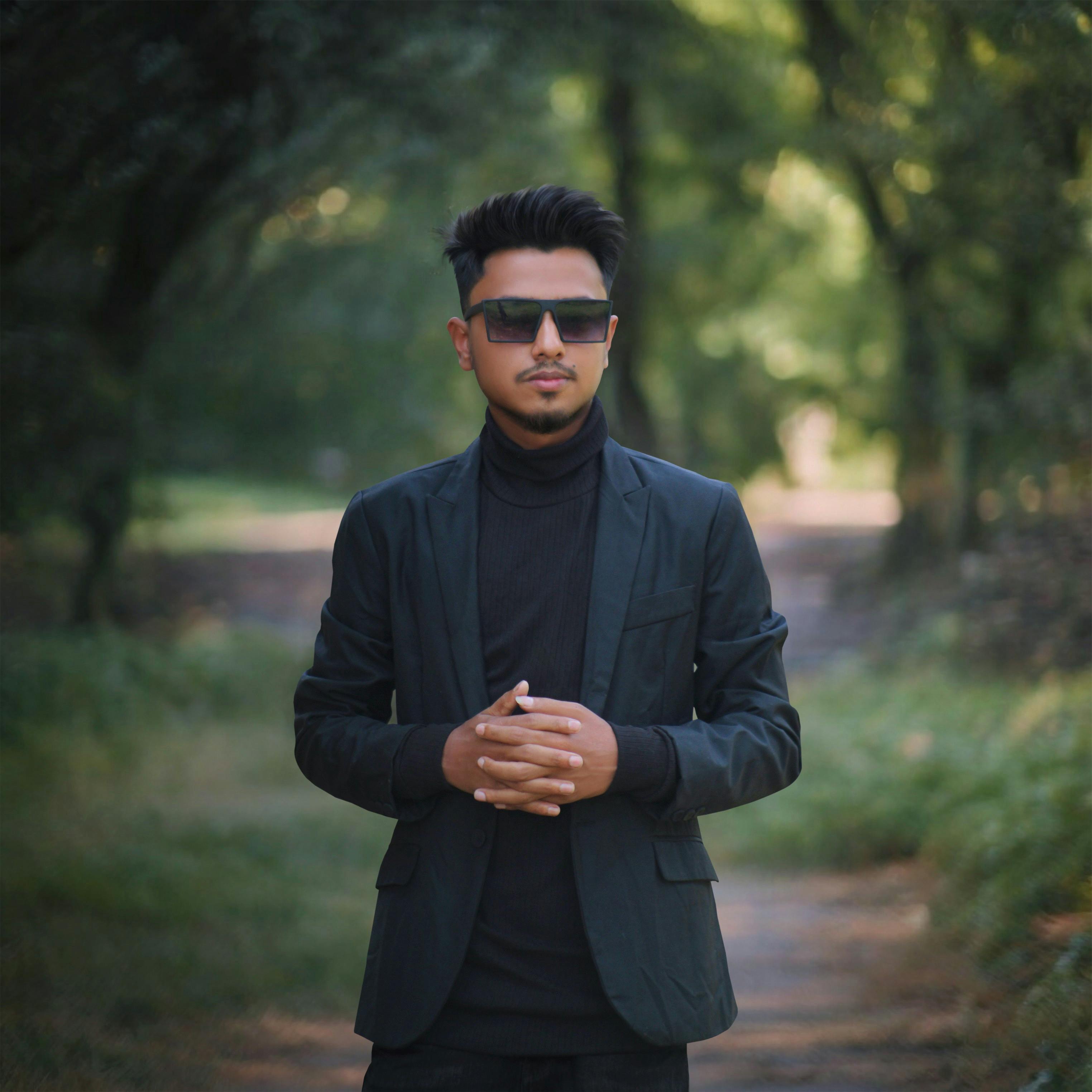 Stylish man in sunglasses and suit standing in a Sylhet forest path during the day.